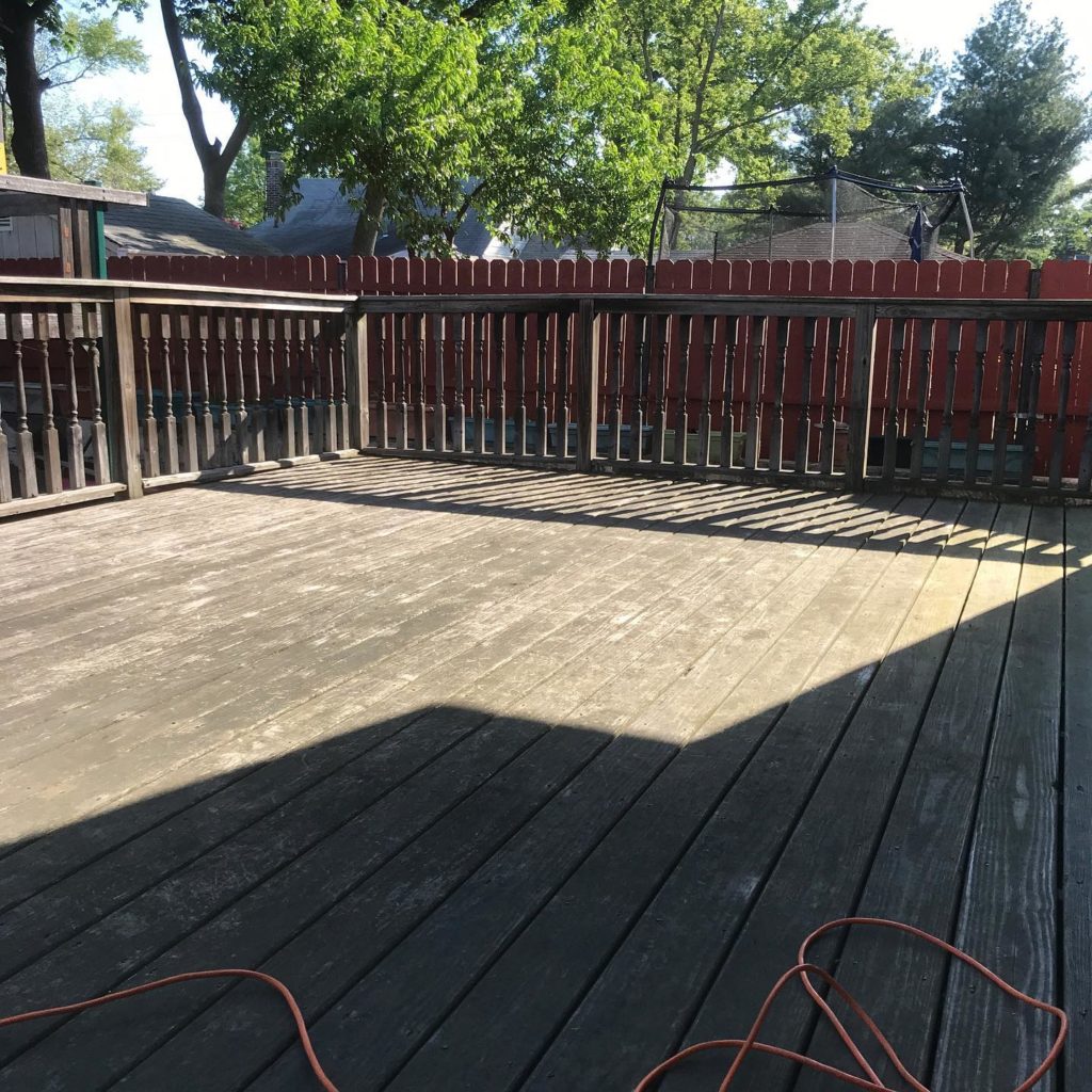 Wooden backyard deck with railing, red fence, and an extension cord on the floor.